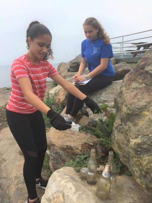 Eighth-grader Fairuz Saleh (left) pulls bottles from a crevice among the rocks while partner Lauren Brooks, also in eighth grade, keeps track of the collection.