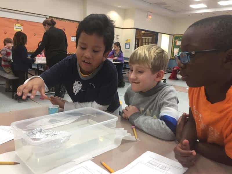 Webster second-graders (from left) Joan Pancho, David Weiss and Aidan Wigfall test the buoyancy of a tinfoil boat with pennies.