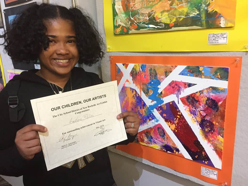Annalize Paulino, a 7th-grader at Isaac E. Young Middle School next to a colorful work she painted. — at New Rochelle Public Library.